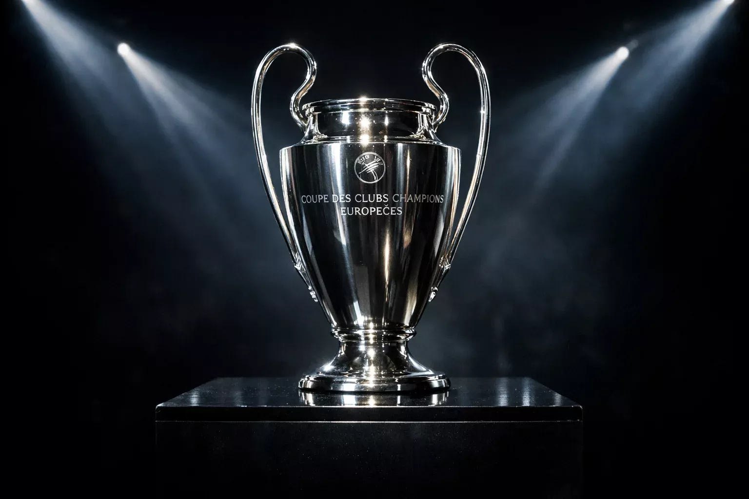 The Champions League trophy displayed on a pedestal under dramatic spotlights
