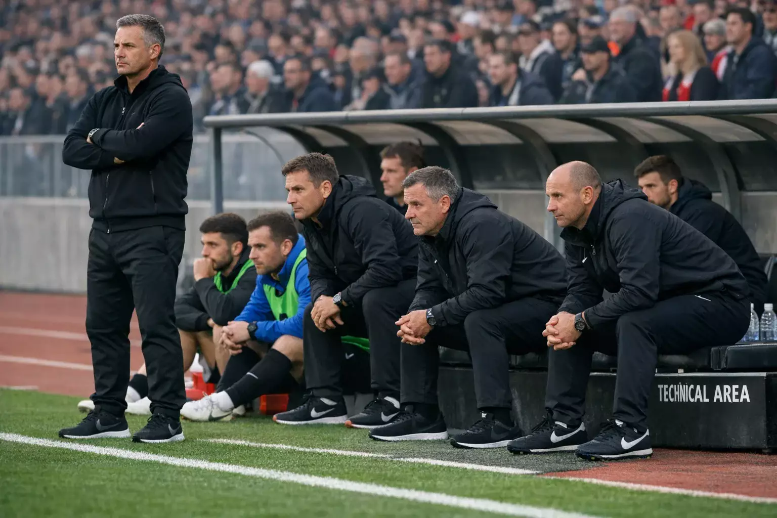 Football players and coaching staff watching anxiously from the sideline during a tense knockout match