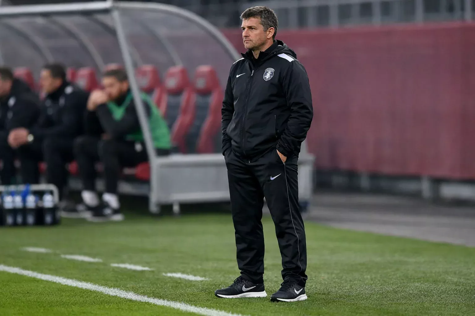 Football manager observing the match intently from the technical area, analyzing tactical patterns