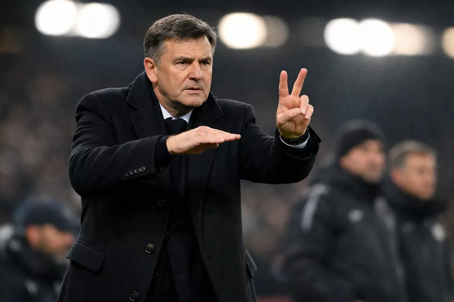 Football manager giving tactical instructions to players on the sideline during a European night match